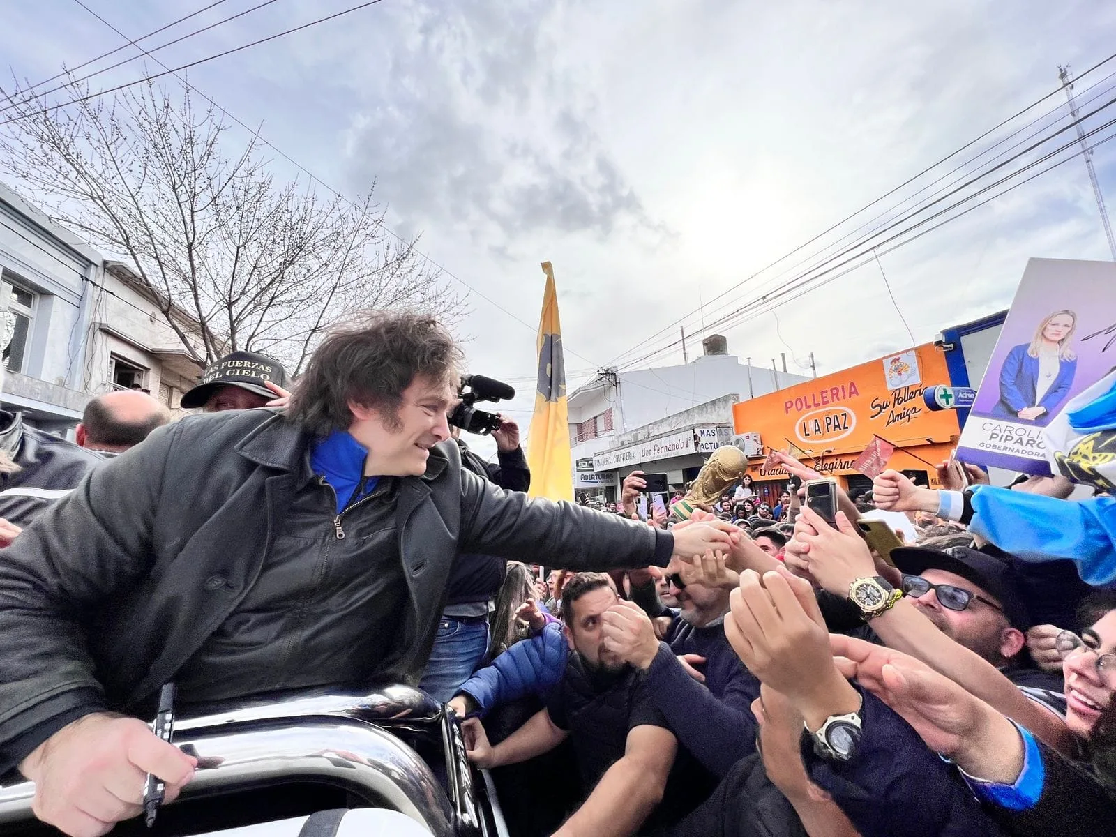 Dirigente saludando a una multitud desde un vehículo en un acto político
